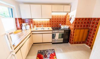 A modern kitchen with a wooden countertop and red tiles. It includes a stove, sink, and refrigerator.