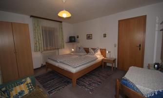 A cozy bedroom with a double bed and wooden dressers. The walls are painted in simple colors, and a rug creates an inviting atmosphere.