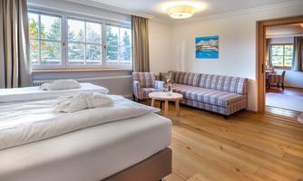 A bright room with a large bed and a cozy sofa. The large windows offer a view of nature.