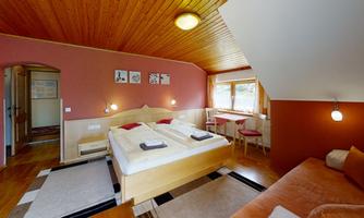 A cozy bedroom with two beds and a wooden ceiling. There is a small table and chairs as well as a sofa in the corner.
