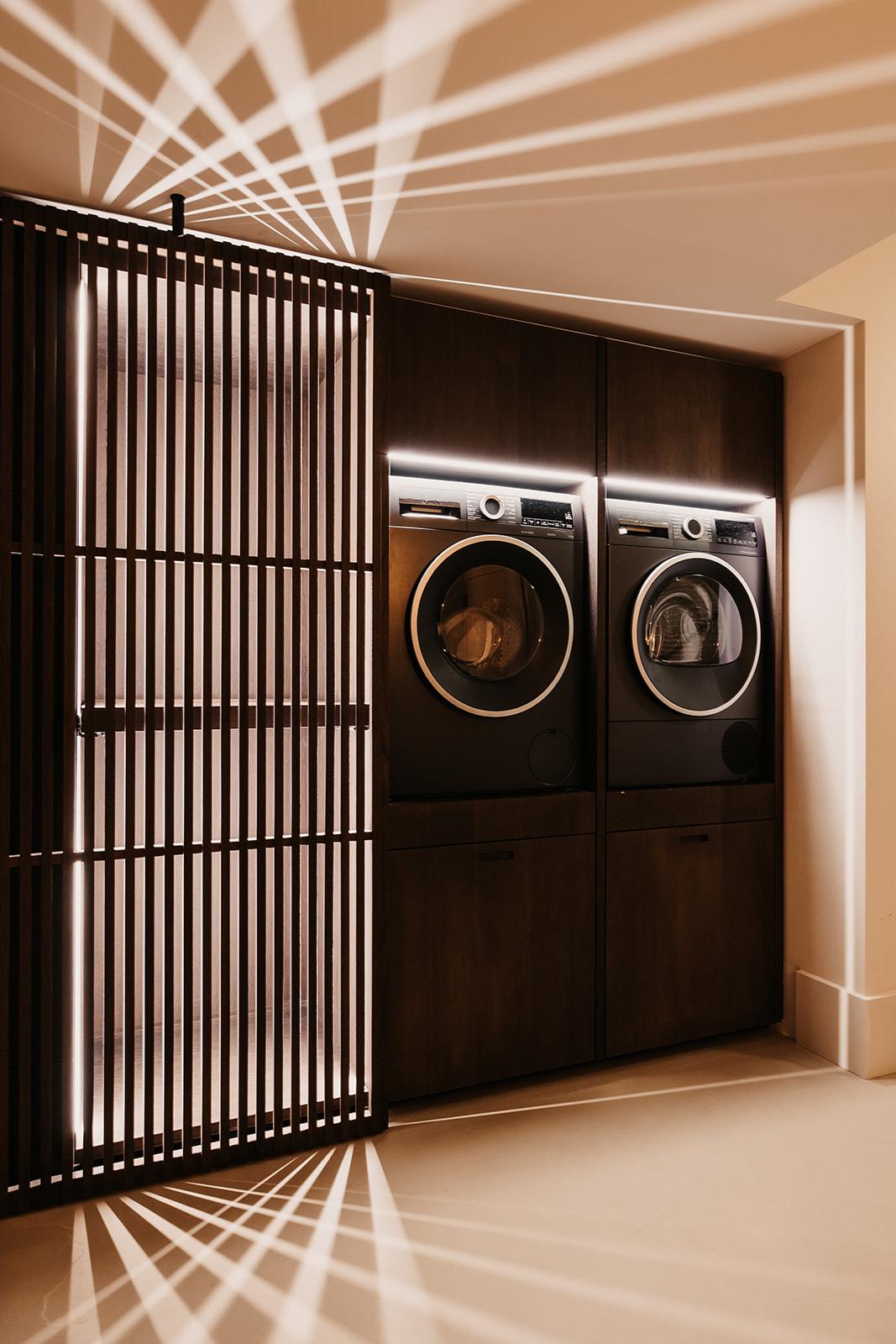 A modern laundry area with two washing machines behind a decorative grid. The room is well lit and has a stylish decor.