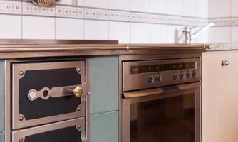 A modern kitchen with a stove, an oven, and cabinets in various colors. The walls are tiled and kitchen utensils hang above the work area.