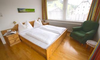 A cozy bedroom with a double bed and two nightstands. The room features large windows and a comfortable armchair.