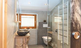 A modern bathroom with a large shower and elegant tiles. A wooden vanity and a window bring in additional light.
