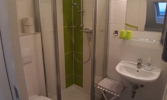 A modern bathroom with a shower cubicle and elegant green accents. There is a sink and a toilet area, everything very bright and clean.