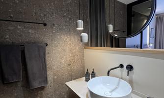 A modern bathroom with an elegant sink and a large mirror. The walls are clad in dark material and there are two towels along with some decorative details.