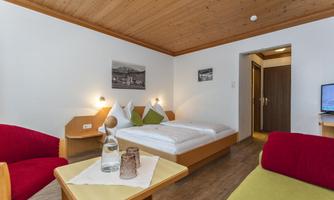 A cozy hotel room with wooden walls and a modern design. It features two beds, a television, and a seating area.