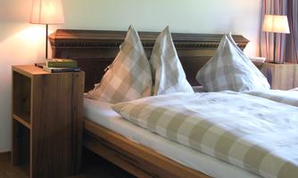 A cozy bedroom with a double bed and decorative pillows. Two skis hang on the wall, and there is soft lighting from the bedside lamps.