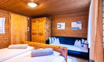 A cozy wooden room with two single beds and a sofa. Modern pictures hang on the wall and the lighting is pleasant.