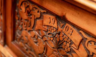 An intricately carved wooden cabinet featuring the year 1903 and a key ring. The detailed work showcases floral patterns and gives the furniture piece a nostalgic charm.