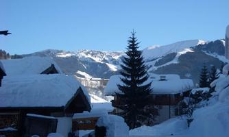 A snowy landscape with cozy cabins and majestic mountains in the background. The clear sky creates a calm and inviting atmosphere.