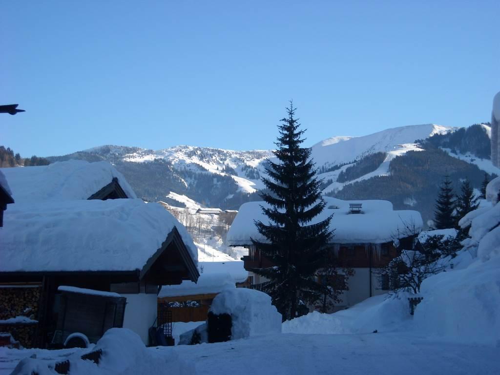 A snowy landscape with cozy cabins and majestic mountains in the background. The clear sky creates a calm and inviting atmosphere.