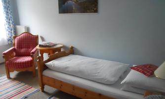 A simple bedroom with a single bed and a red armchair. There is a colorful rug and a picture on the wall.