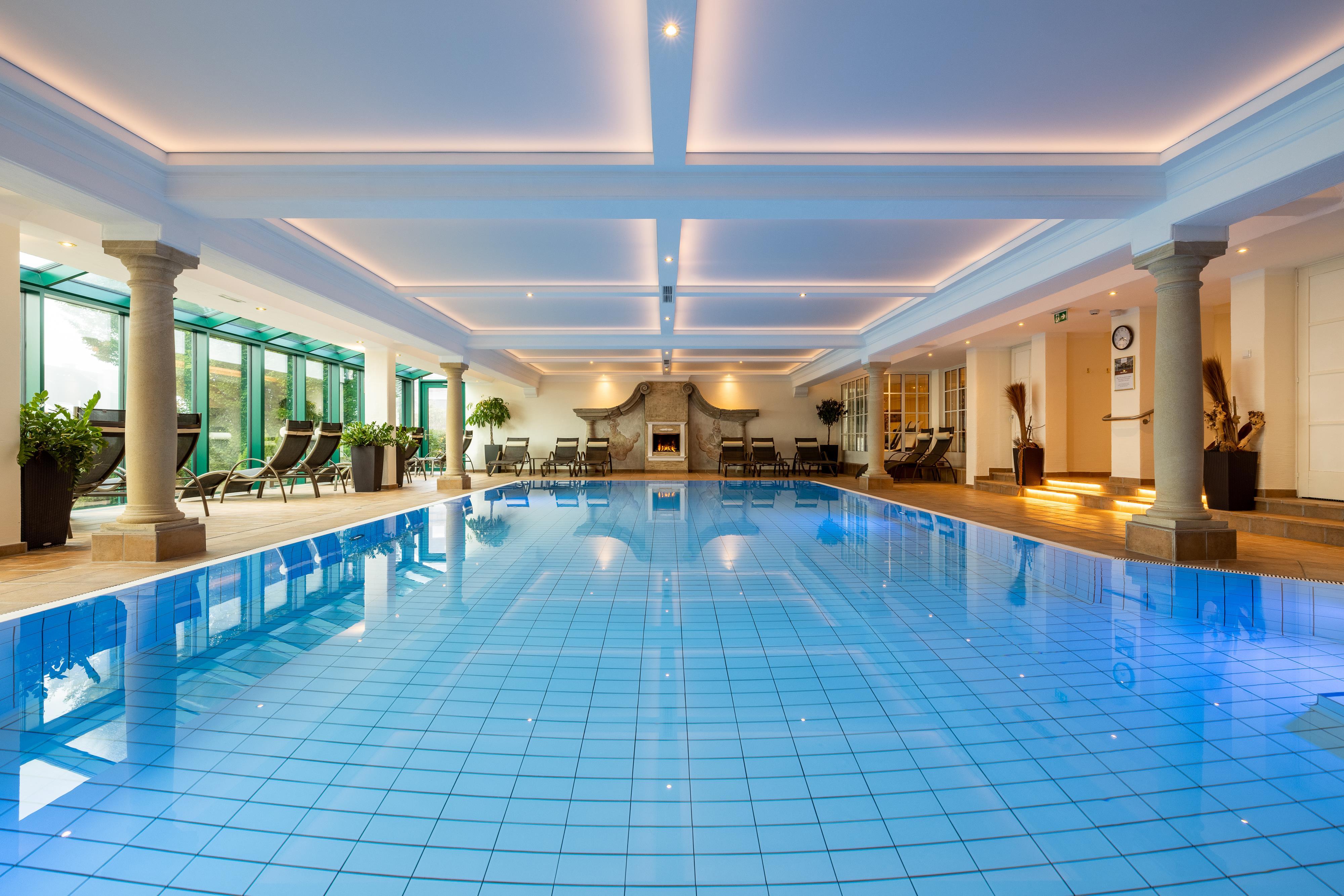 An elegant indoor pool with clear water and blue tiles. The pleasant lighting and the plants create a relaxing atmosphere.
