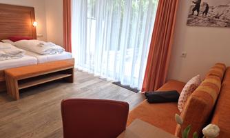 A cozy room with a double bed and a sofa. Large windows let in plenty of light and offer a view outside.