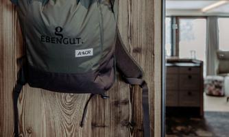 A backpack is hanging on a wooden wall. In the background, a modern room can be seen.