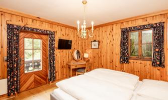 A cozy bedroom with wooden paneling and a large window. The room is furnished with a double bed and a small desk.