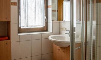 A modern bathroom with tiles and wooden cabinets. There is a shower, a sink, and a window with curtains.