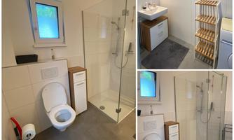 A modern bathroom with a glass shower cubicle, a sink, and a toilet. The walls are tiled in light colors and there is a simple wooden shelf.