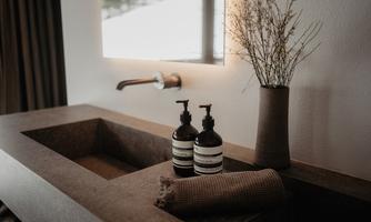 A modern bathroom with a stylish wash basin. On the shelf are two black soap dispensers and a decorative flower pot.