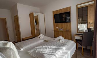 A modern hotel room with two twin beds and bright wooden interiors. A television as well as a desk are also available in the room.