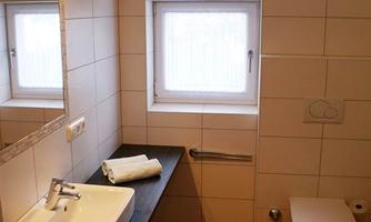 A modern bathroom with a sink, a large mirror, and a toilet. The walls are tiled and the floor has brown tiles.