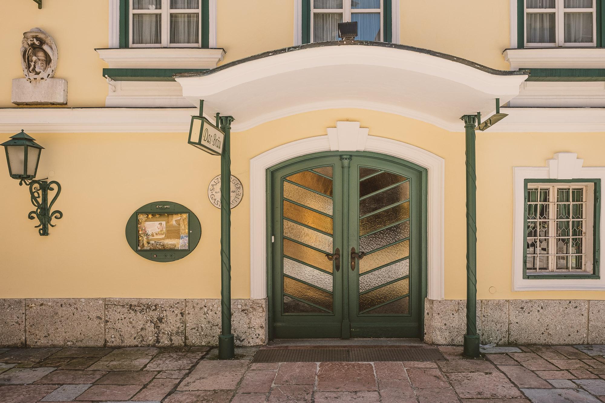 A charming entrance door in a yellow building with green accents. Next to the door is a wrought iron light and a round window.