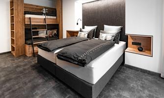 A modern bedroom with a double bed and a bunk bed. The decor is stylish with wood and neutral colors.