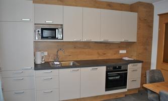 A modern kitchen with light cabinets and a kitchenette. It is equipped with a refrigerator, microwave, and stove.