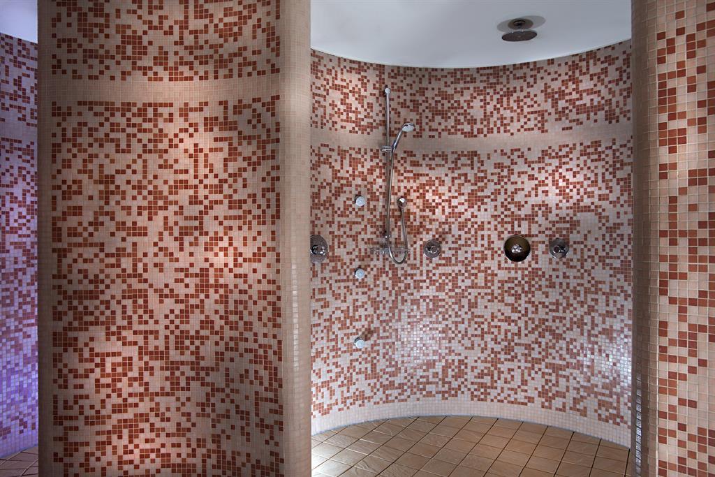A modern shower area with colored tiles and multiple showerheads. The walls are round and create a unique atmosphere.