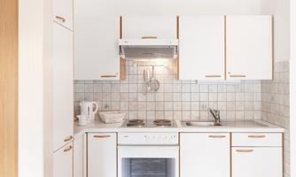 A bright and modern kitchen with white cabinets and a tile backsplash. The space is well-organized with a stove, sink, and various kitchen appliances.