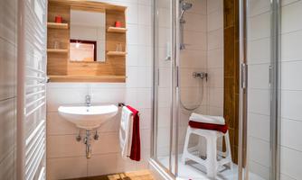 A modern bathroom with a shower and a white sink. The walls are light-tiled, and there are wooden elements for a warm accent.
