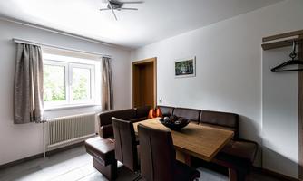 A cozy dining area with a wooden table and upholstered chairs. The room is bright and well-lit, with a window overlooking the outdoor landscape.
