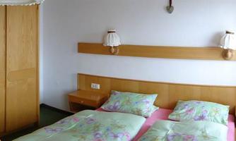 A simple room with two beds and colorful bedding. There is a wardrobe and a window with checked curtains.