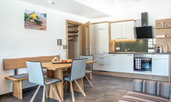 A modern kitchen with a wooden dining area and elegant chairs. The space is bright and friendly designed, featuring medium wood and gray tones.