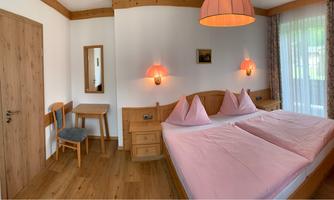 A cozy room with wooden decor and a double bed. Large windows provide plenty of daylight.