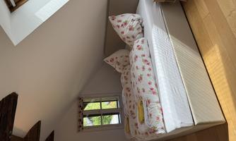 A cozy bedroom with a large bed and floral bed covers. The room has a window that lets in a lot of natural light.