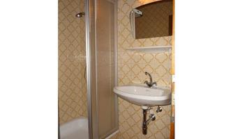 A small bathroom with a shower cubicle and a sink. The walls are decorated with orange patterned wallpaper.