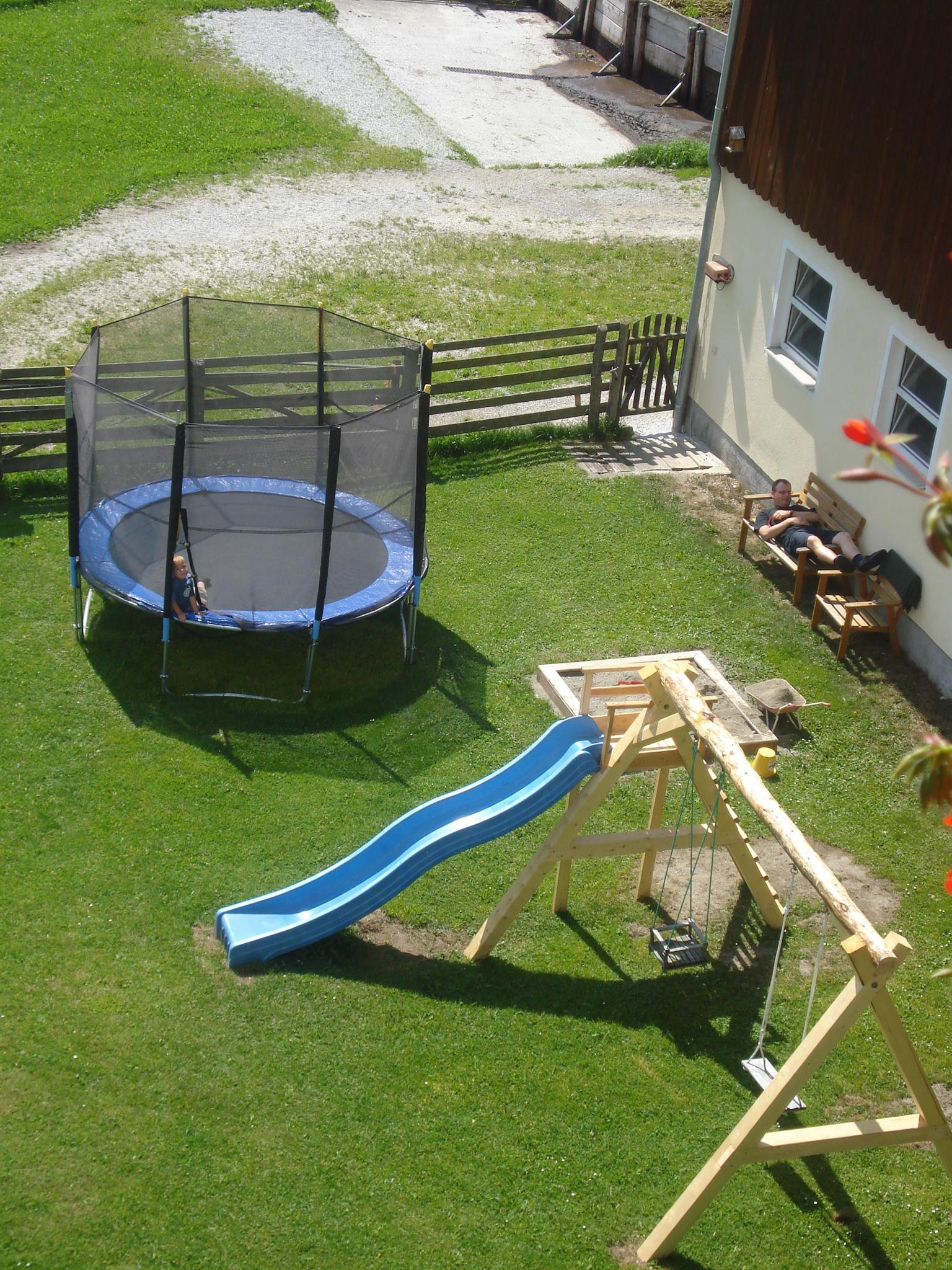 A garden with a trampoline and a slide. In the background, a play tower is visible.