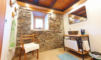 A modern bathroom with stone walls and wooden ceilings. There is a wooden cabinet with a sink and a chair.