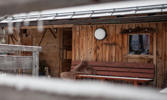 A cozy wooden cabin in the snow with a snow-covered bench in front of the door. The image conveys a calm, wintry atmosphere.