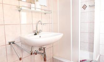 A simple bathroom with a shower and a sink. The walls are tiled and the floor is covered with red tiles.