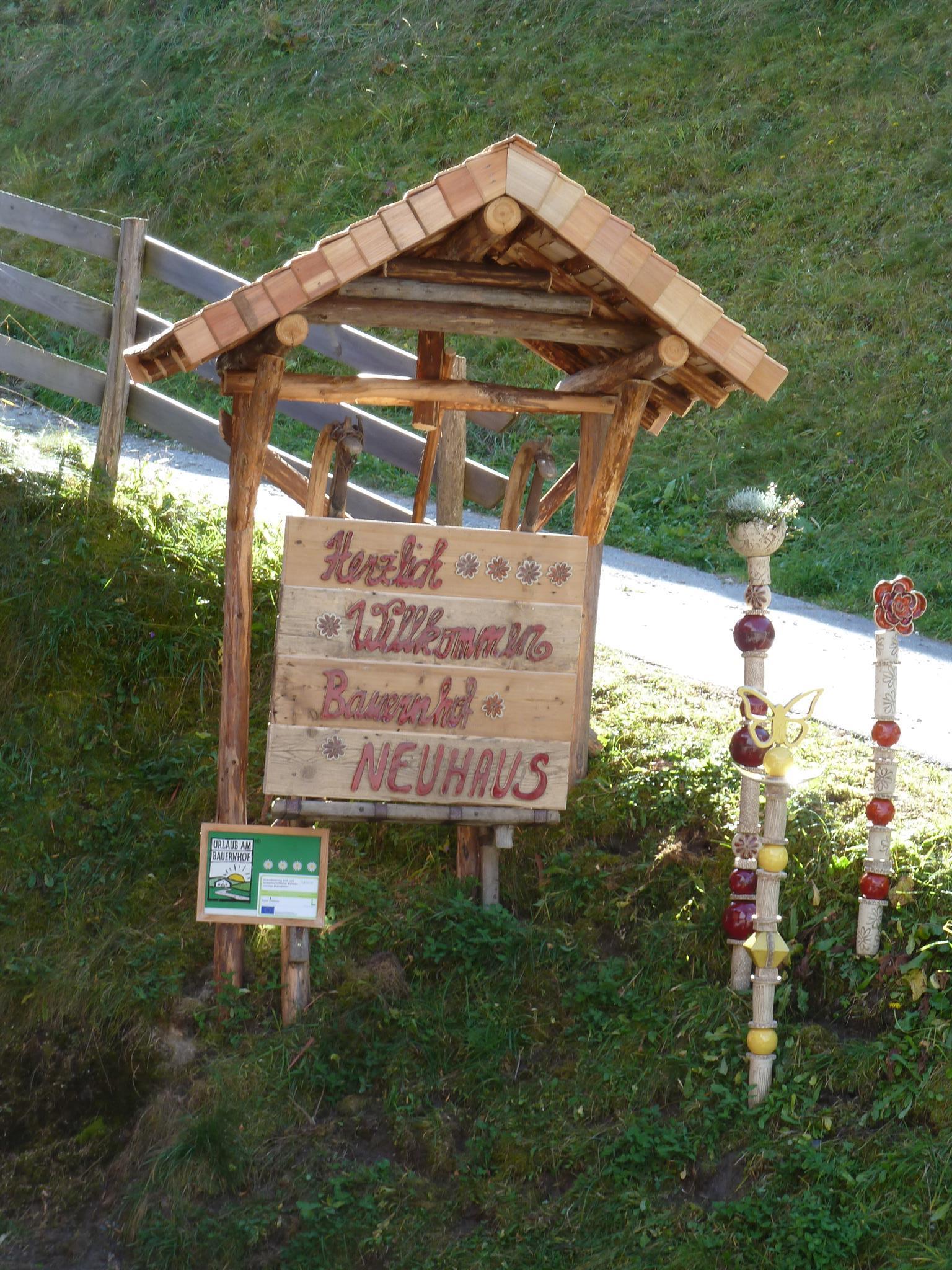 A wooden sign with the inscription "Ferienwohnung Baumann" and "Neuhaus" stands under a small roof. Next to it are decorative, creatively designed posts.