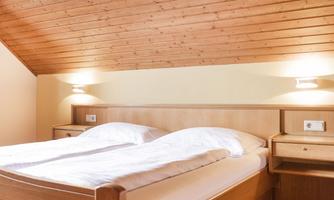 A cozy bedroom with a double bed and wooden paneling. There are nightstands and soft lighting on the walls.