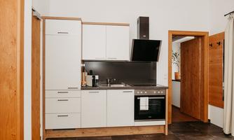 A modern kitchen with white cabinets and a cooktop. The room features warm wood tones and an elegant, minimalist look.