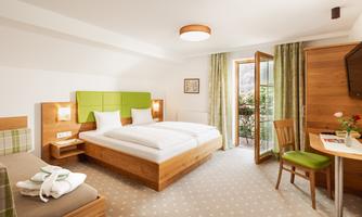 A modern hotel room with a double bed and a cozy chair. Large windows provide plenty of daylight and offer access to a small balcony.