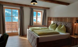 A modern bedroom with a double bed and large windows. The room offers a beautiful view of the mountains and has a warm, inviting atmosphere.