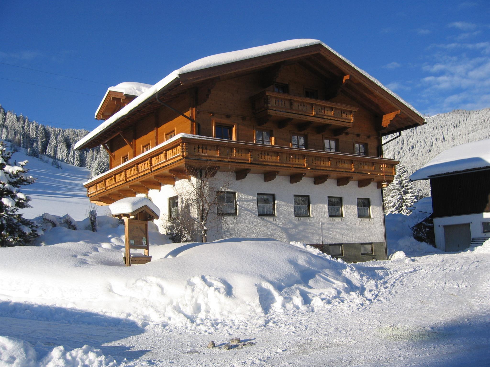 A beautiful wooden house in winter, surrounded by a lot of snow. The clear blue sky complements the winter landscape.
