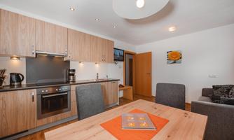 A modern kitchen with wooden cabinets and an elegant countertop. The dining area is cozy, furnished with a wooden table and gray chairs.