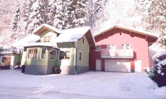 Two charming houses in the snow, surrounded by snow-covered trees. The sun is shining and creates a warm atmosphere.